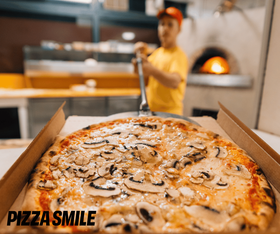 pizza che entra nella scatola per il delivery, pizzaiolo e forno a legna sullo sfondo